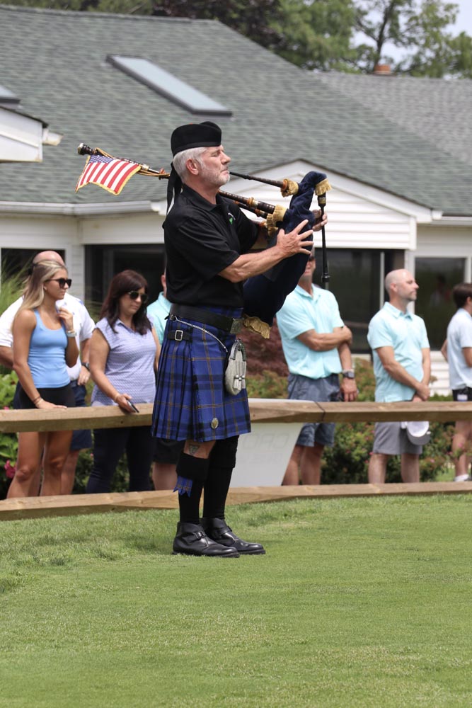 Man in traditional clothing plays a bag pipe.