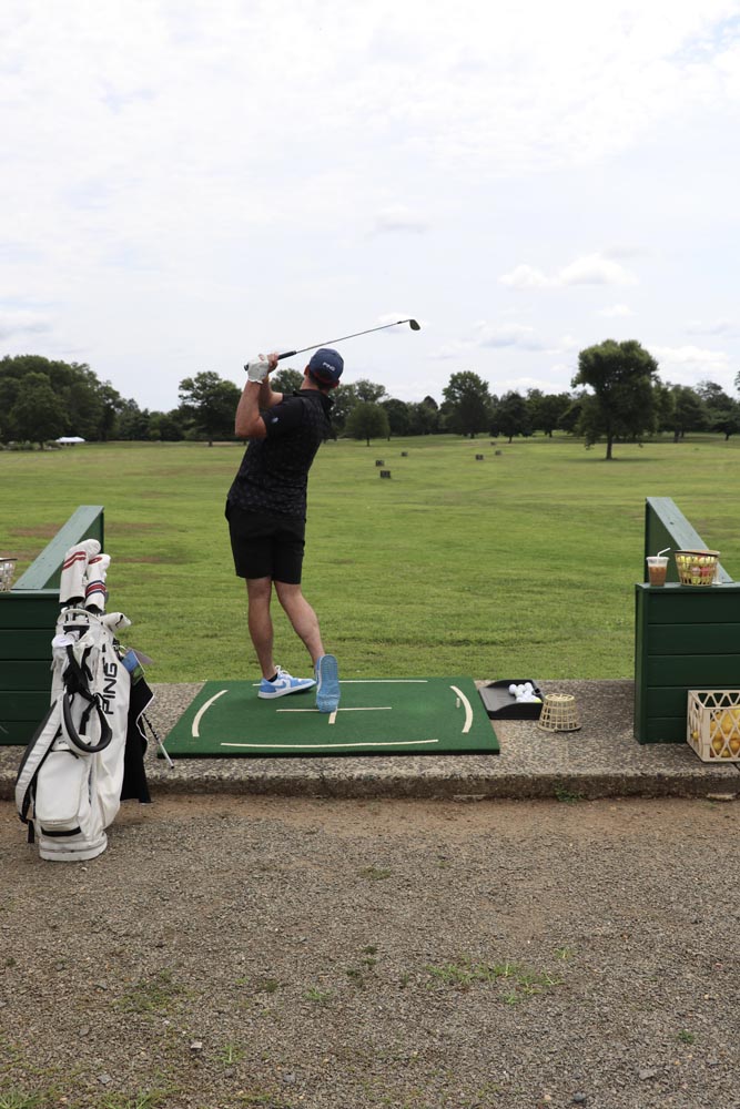 Driving range view from the stands. A golfer finishes his swing.